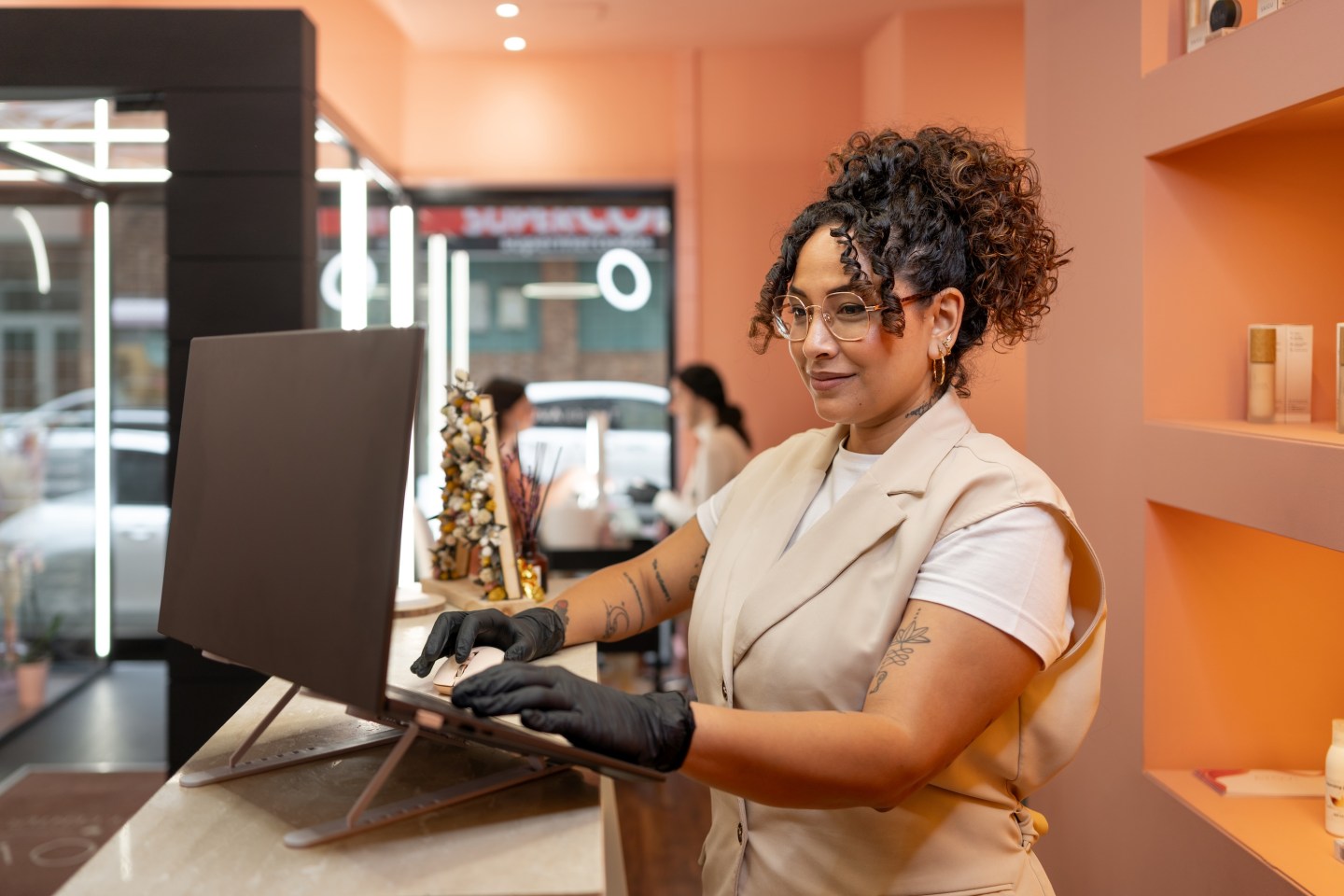 Stylish beautician in black gloves working on a laptop at the front desk of a beauty salon, scheduling appointments