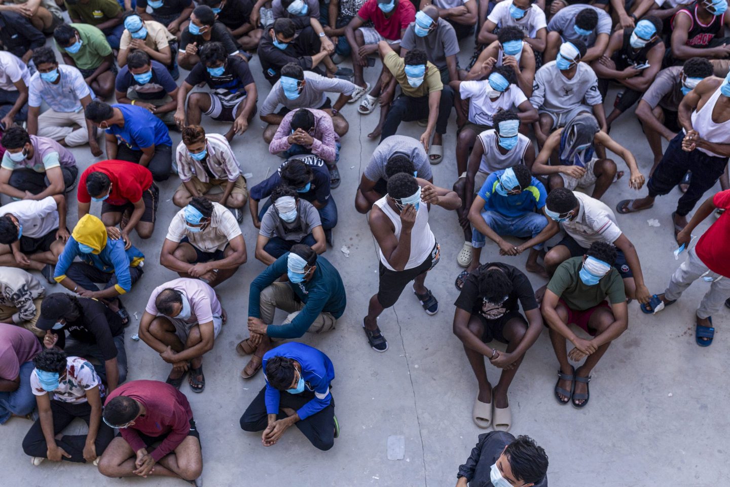 people with masks over their faces sit cross-legged, crowded next to each other