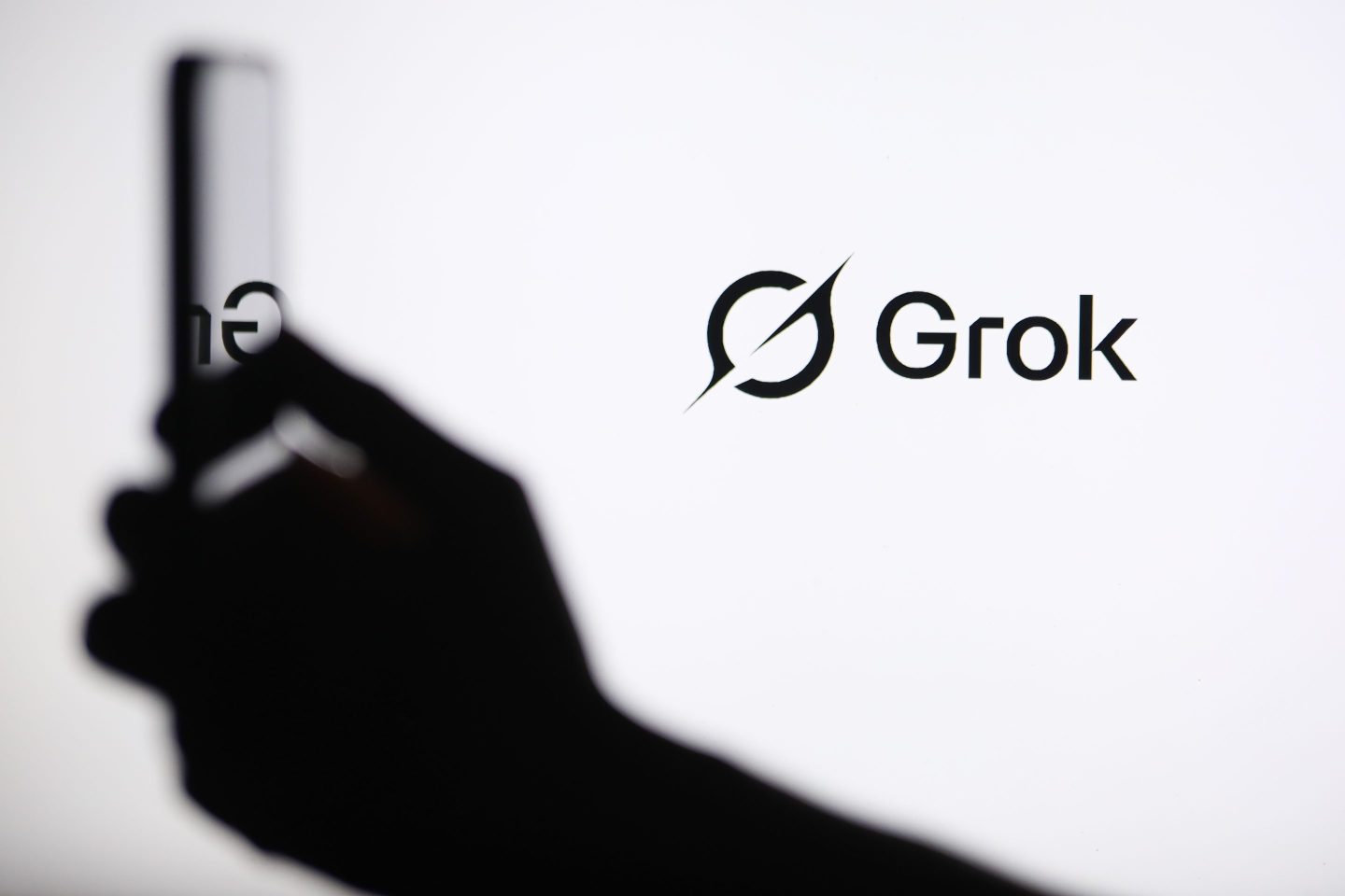 A screen displays the Grok logo while a person holds another phone in front.
